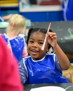 Student holding up a paintbrush and smiling