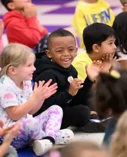 Students clapping, cross-legged on the floor