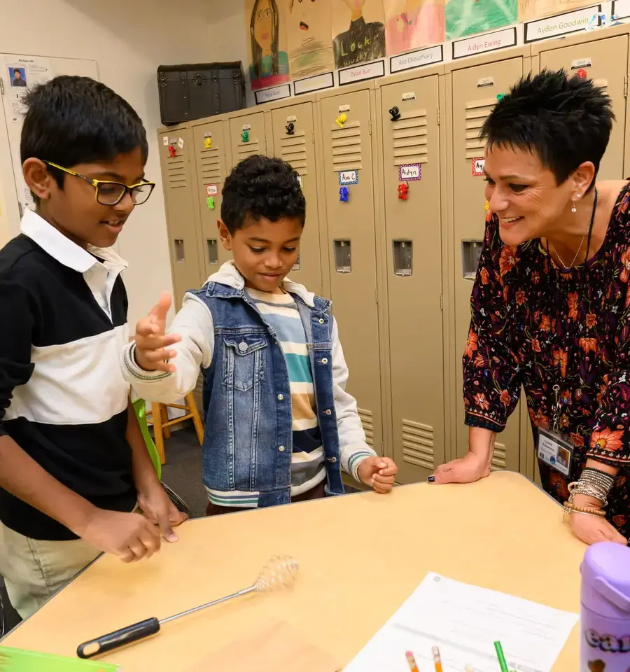 Teacher standing with two students at table